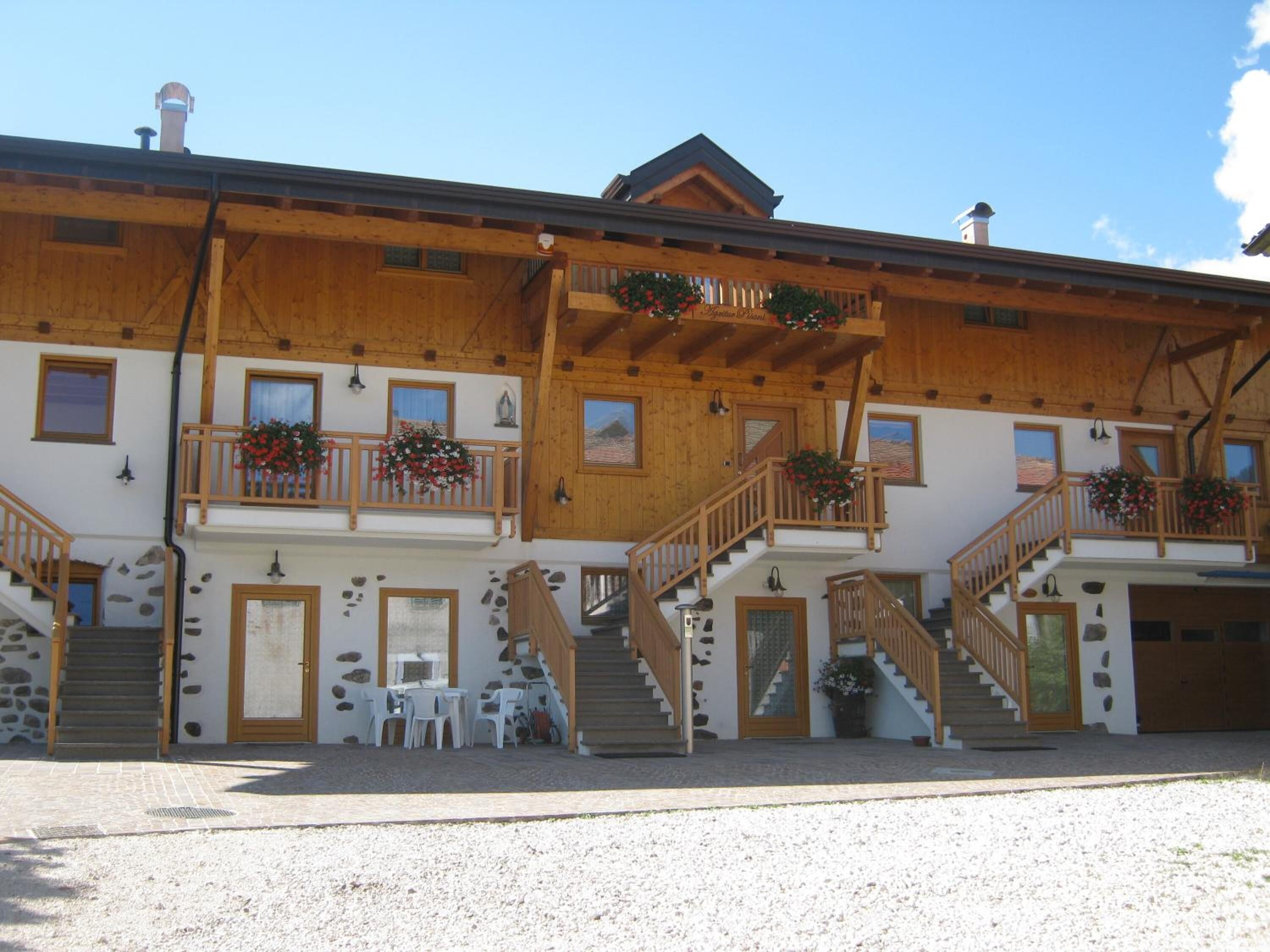 A two-story wooden building with balconies, stone walls, and a gravel driveway.