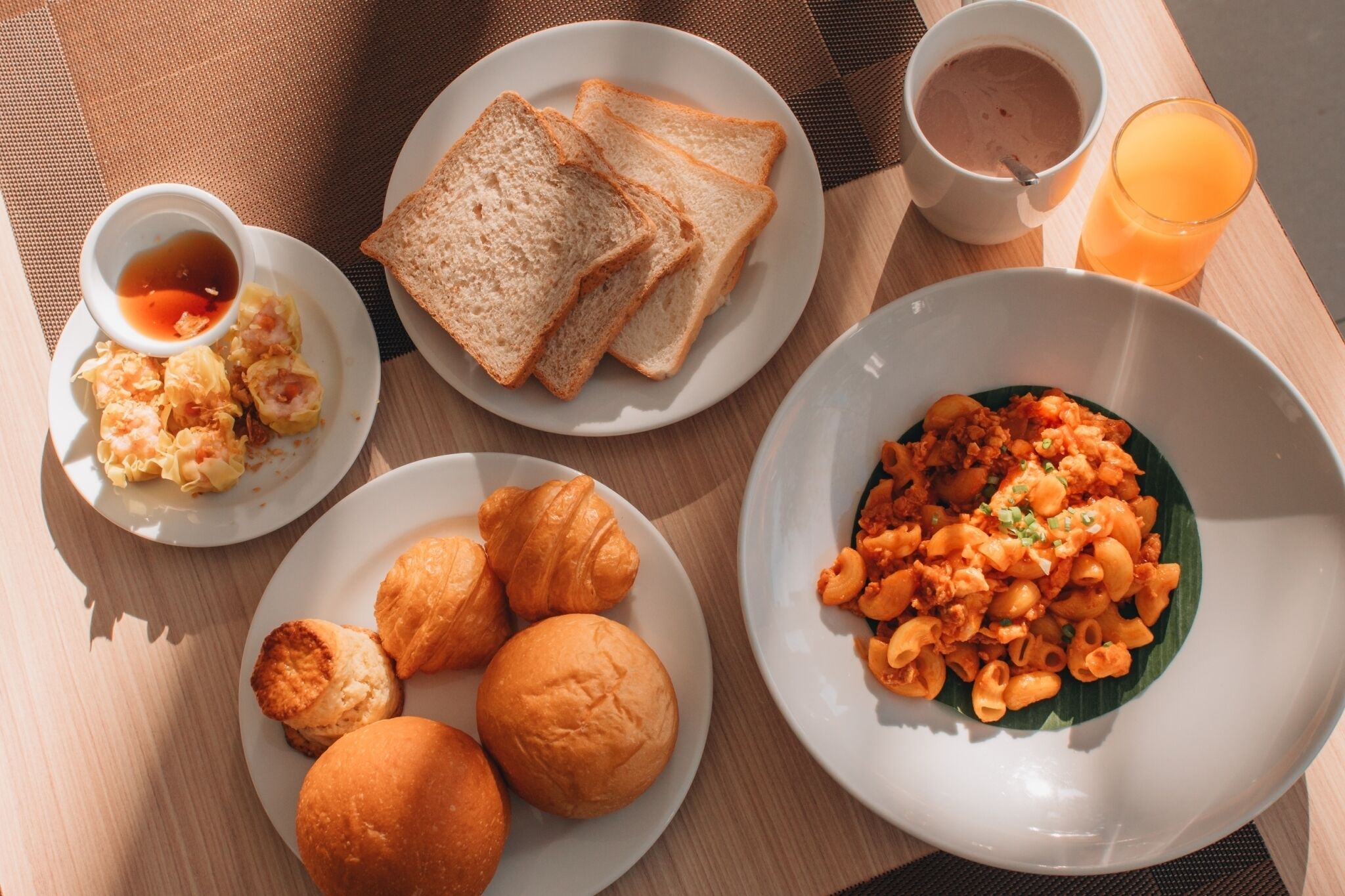 A breakfast tray with toast, croissants, biscuits, macaroni salad, and a cup of coffee.