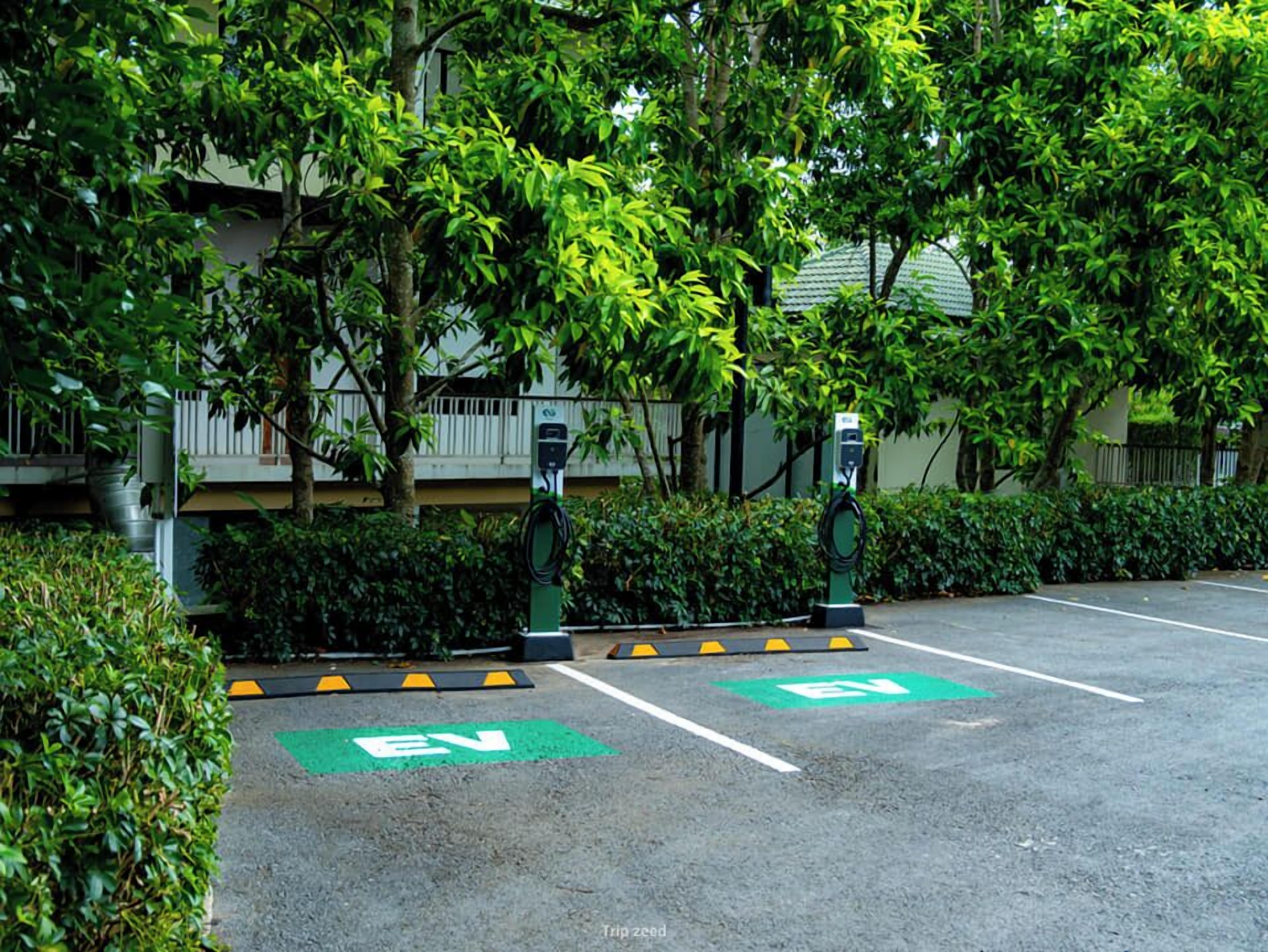 An electric vehicle charging station in a parking lot with green EV parking spaces and a building in the background.