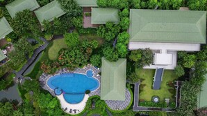 An aerial view of a residential area with a large swimming pool, multiple green-roofed buildings, and lush greenery. - Vivace Khaoyai Resort (Pak Chong)