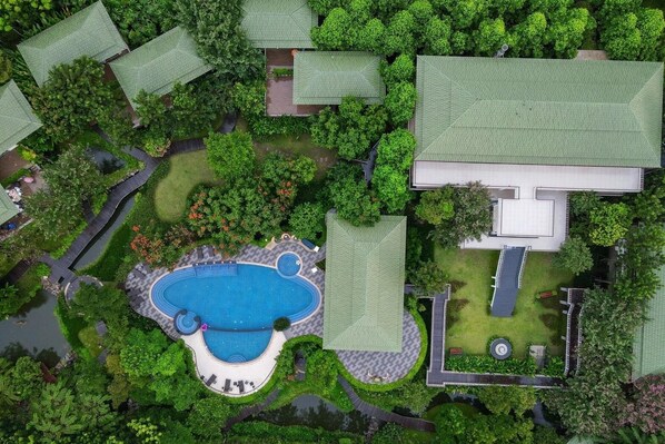 Una vista aerea di una zona residenziale con una grande piscina, diversi edifici con tetti verdi e una vegetazione rigogliosa.