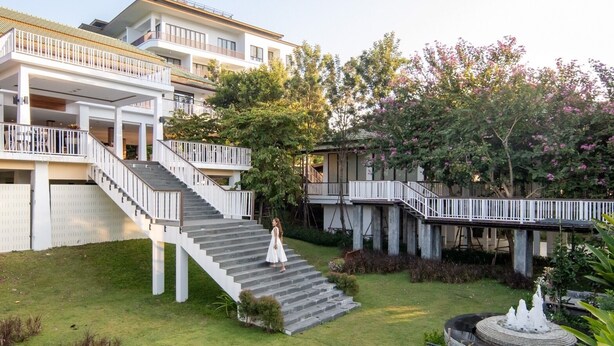 A multi-story building with a central staircase, outdoor seating area, and a garden with a fountain. - Vivace Khaoyai Resort (Pak Chong)