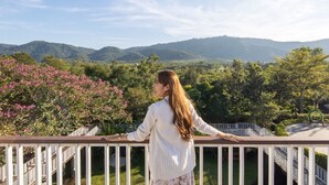 A person standing on a balcony with a view of green hills and pink flowers. - Vivace Khaoyai Resort (Pak Chong)