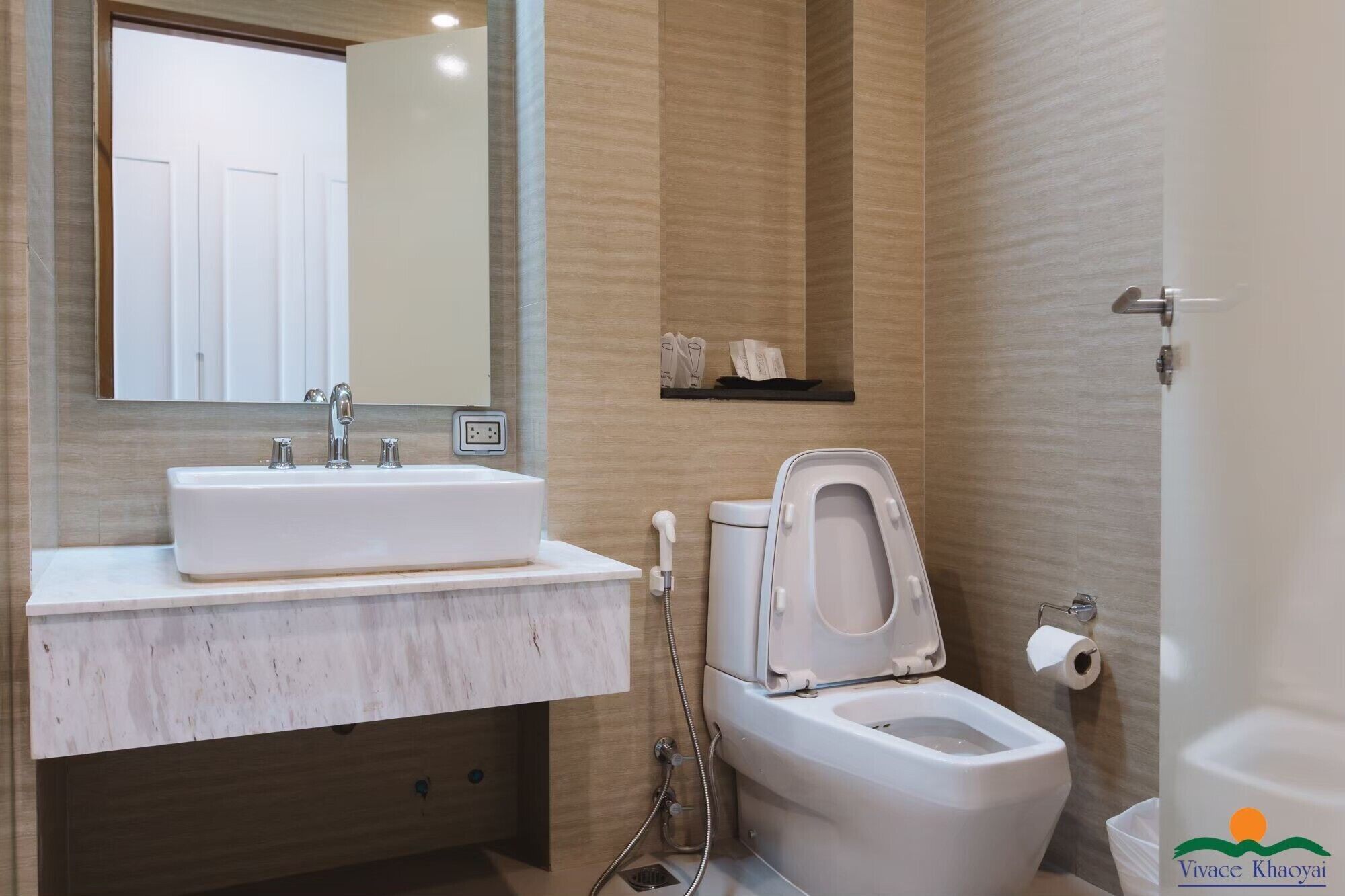 A bathroom with a white sink, mirror, and toilet. There is a shelf above the toilet with toiletries.