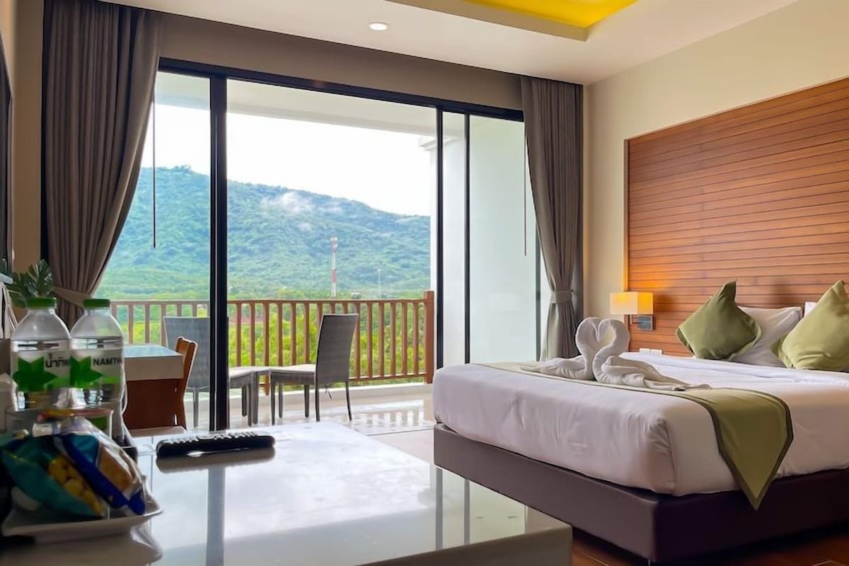 Habitación de hotel con una cama, un escritorio con un control remoto, una mesa con una planta y vistas a un paisaje montañoso.