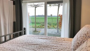A bedroom with a bed, a window with curtains, and a view of a green field and trees. - Lovely home in Baarle-Nassau (Baarle-Nassau)