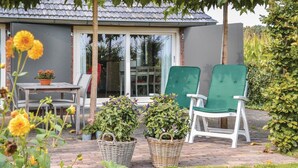 A patio with a table and two green chairs, surrounded by potted plants and a house in the background. - Lovely home in Baarle-Nassau (Baarle-Nassau)