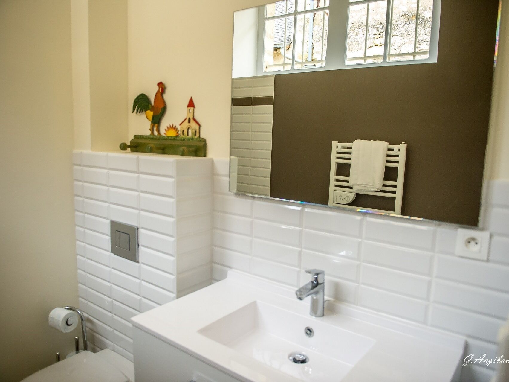 A bathroom with white tiled walls, a white sink, a mirror, and a window with blinds.