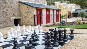 A large outdoor chessboard set up on a gravel surface with a stone building in the background. - En Rou Libre (Rou-Marson)