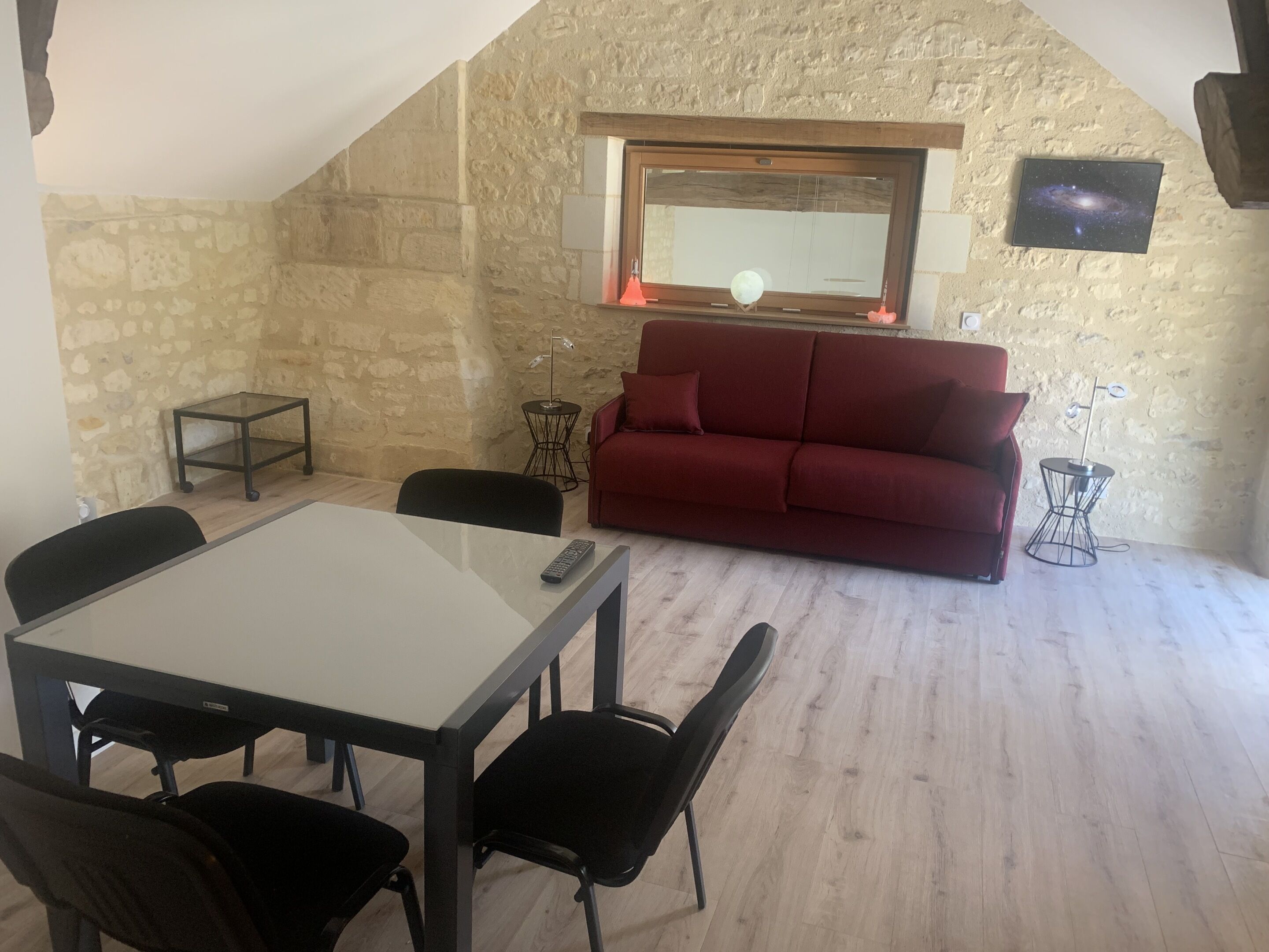 A cozy living room with a red sofa, a dining table with chairs, a small side table, and a television mounted on the wall.
