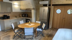 A compact kitchen with a dining area, featuring a wooden table, chairs, and a refrigerator. - En Rou Libre (Rou-Marson)