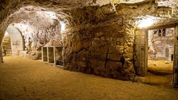Un interior que recuerda a una cueva, con paredes de piedra, una puerta de madera y un estante con botellas.