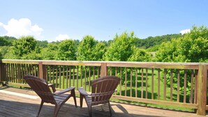 A wooden deck with two Adirondack chairs and a small table, overlooking a lush green landscape.