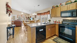 A kitchen with wooden cabinets, a black dishwasher, a stove, and a microwave. There is a dining area with a table and chairs.