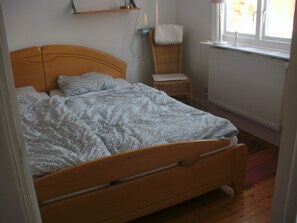 A wooden bed with a patterned blanket, a chair with a white cushion, and a radiator in a room with wooden flooring. - Quietly located cozy vacation home with a view, sauna and wood-burning stove (Ruda)