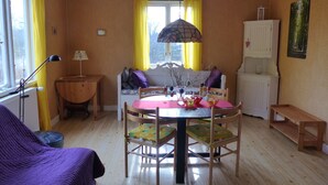 A dining area with a round table, chairs, a lamp, and a window with yellow curtains. - Quietly located cozy vacation home with a view, sauna and wood-burning stove (Ruda)