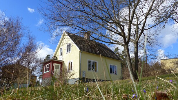 A two-story house with a sloped roof, surrounded by grass and trees. - Quietly located cozy vacation home with a view, sauna and wood-burning stove (Ruda)