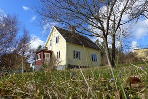 A two-story house with a sloped roof, surrounded by grass and trees. - Quietly located cozy vacation home with a view, sauna and wood-burning stove (Ruda)
