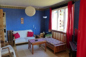A room with a blue wall, a white sofa, a wooden bed, a small table with a patterned tablecloth, and a red curtain. - Quietly located cozy vacation home with a view, sauna and wood-burning stove (Ruda)