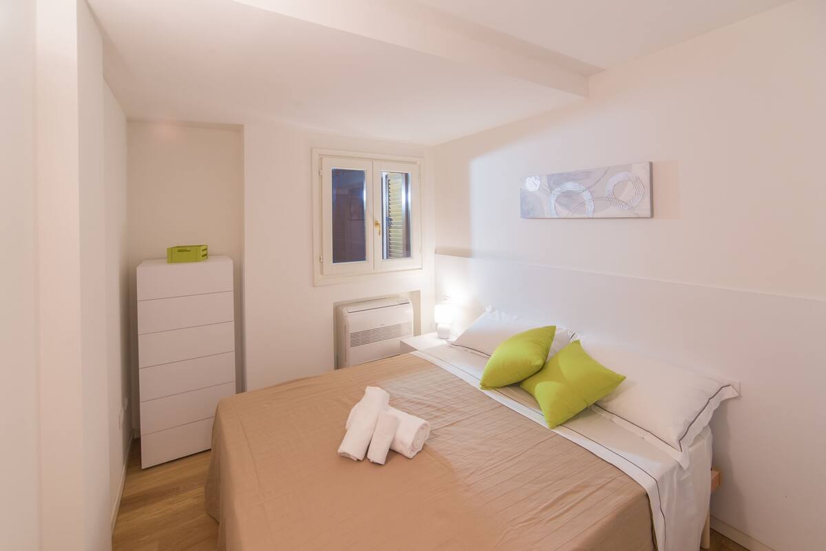 Una camera da letto con un letto, una finestra, un termosifone e un'opera d'arte appesa al muro.