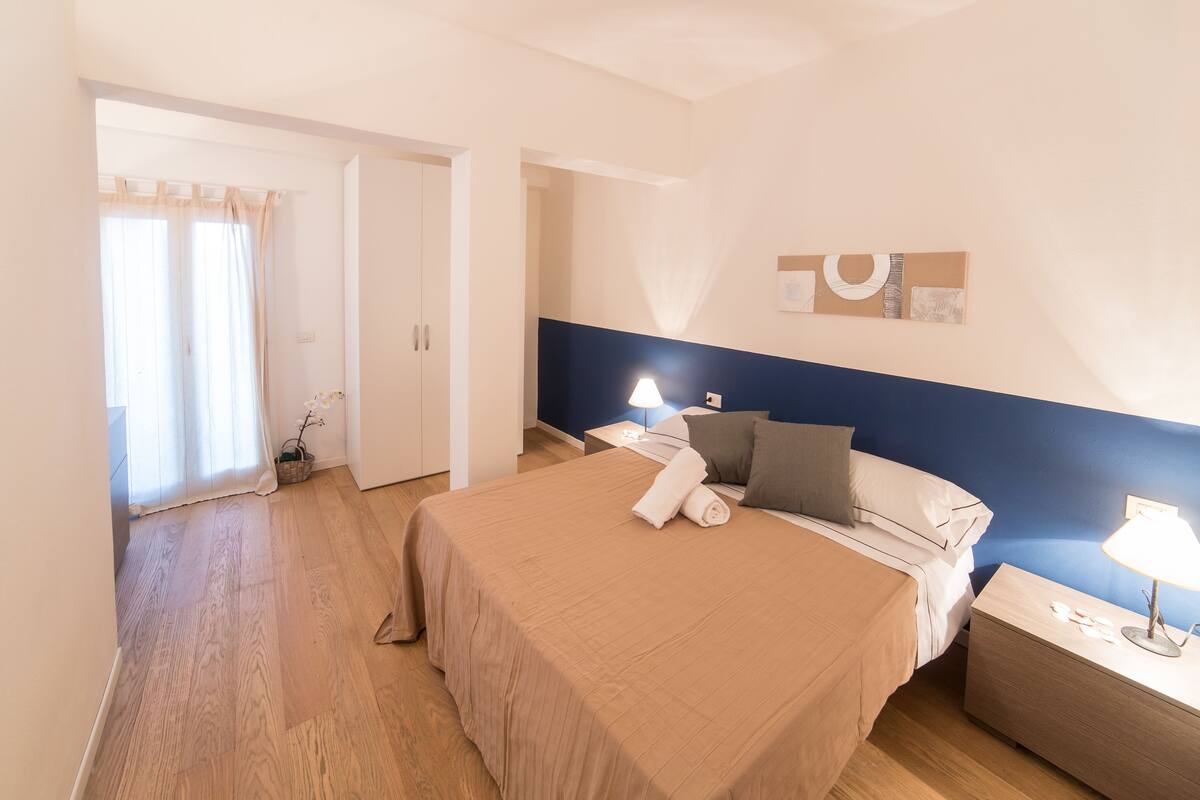 Una camera da letto con un letto, comodini, una lampada e una finestra con tende.