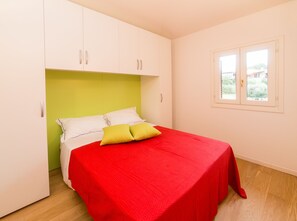 A bedroom with a bed, green headboard, white cabinets, and a window with a view of greenery.
