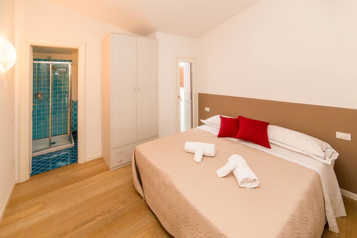 Una camera d'albergo con un letto, un armadio, un bagno con doccia e una porta che dà su un'altra stanza.