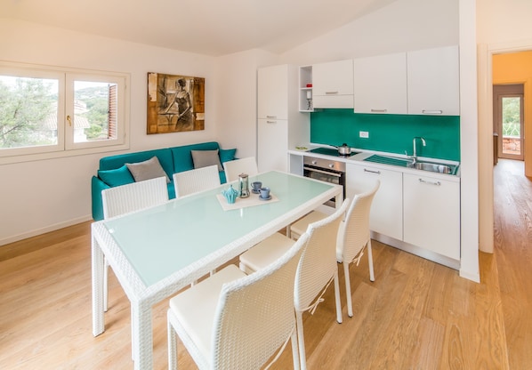 A modern kitchen with white cabinets, a green backsplash, and a dining area with a glass table and white chairs.