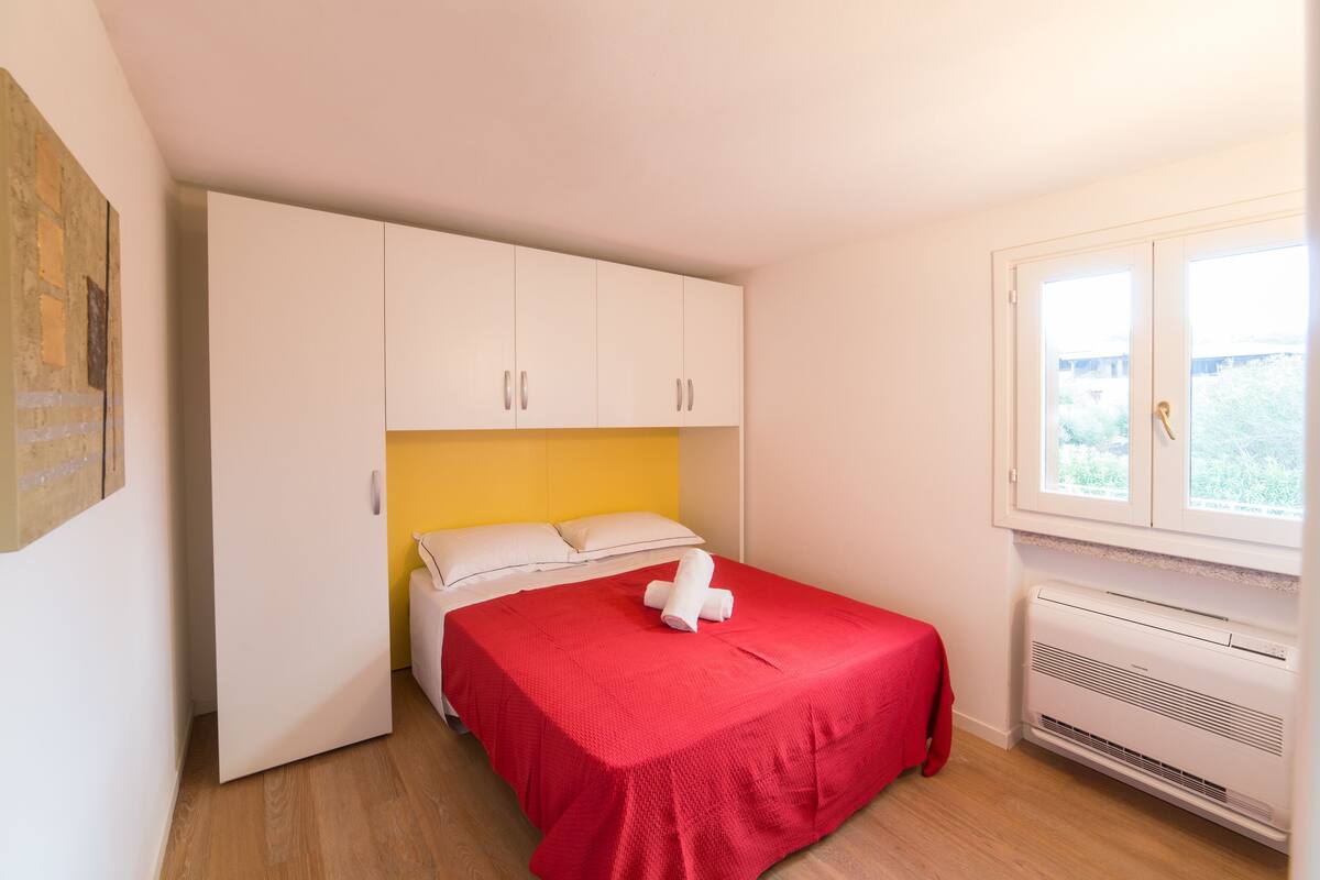 Una camera da letto con un letto, mobili bianchi, una coperta rossa e una finestra vista.