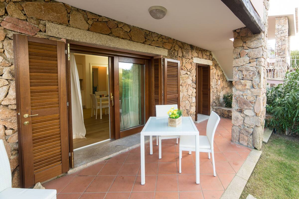 Un patio con tavolo e sedie bianche, un muro in pietra e persiane di legno.