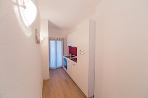 A narrow hallway leading to a kitchen with white cabinets and a red accent wall.