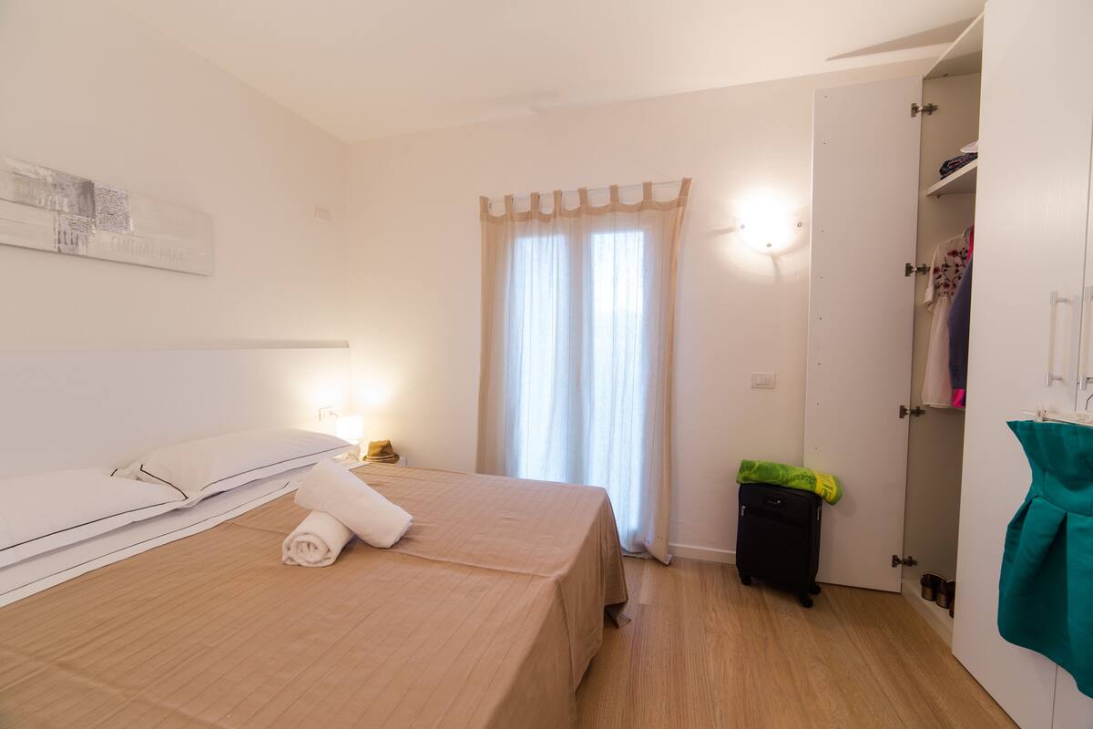Una camera d'albergo con un letto, un armadio, una valigia e una finestra con tende.