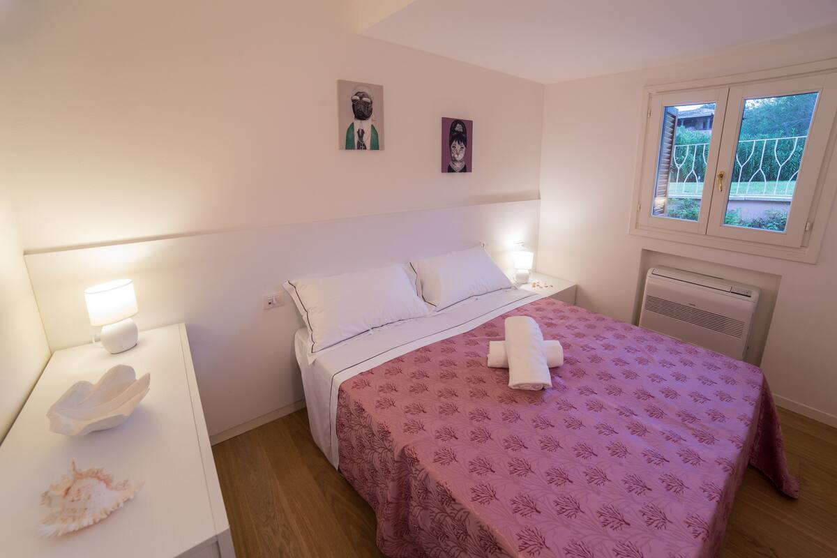 Una camera da letto con un letto, comodini, una finestra e opere d'arte alle pareti.