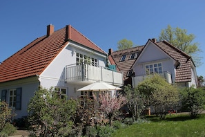 A two-story house with a balcony, a garden with flowering plants, and a red-tiled roof. - Abels Strandkoje, Germany (Wustrow)