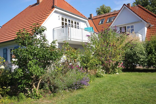 A two-story house with a red-tiled roof, a balcony, and a well-maintained garden with various plants and flowers.