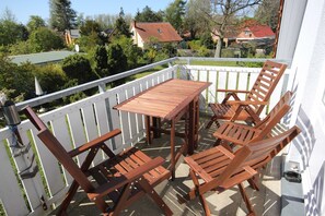A balcony with a wooden table and chairs, white railing, and a view of houses and trees. - Abels Strandkoje, Germany (Wustrow)