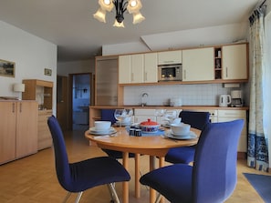 A compact kitchen with a microwave, toaster, and coffee maker. There is a dining table with chairs and a small cabinet with a sink. - Abels Strandkoje, Germany (Wustrow)