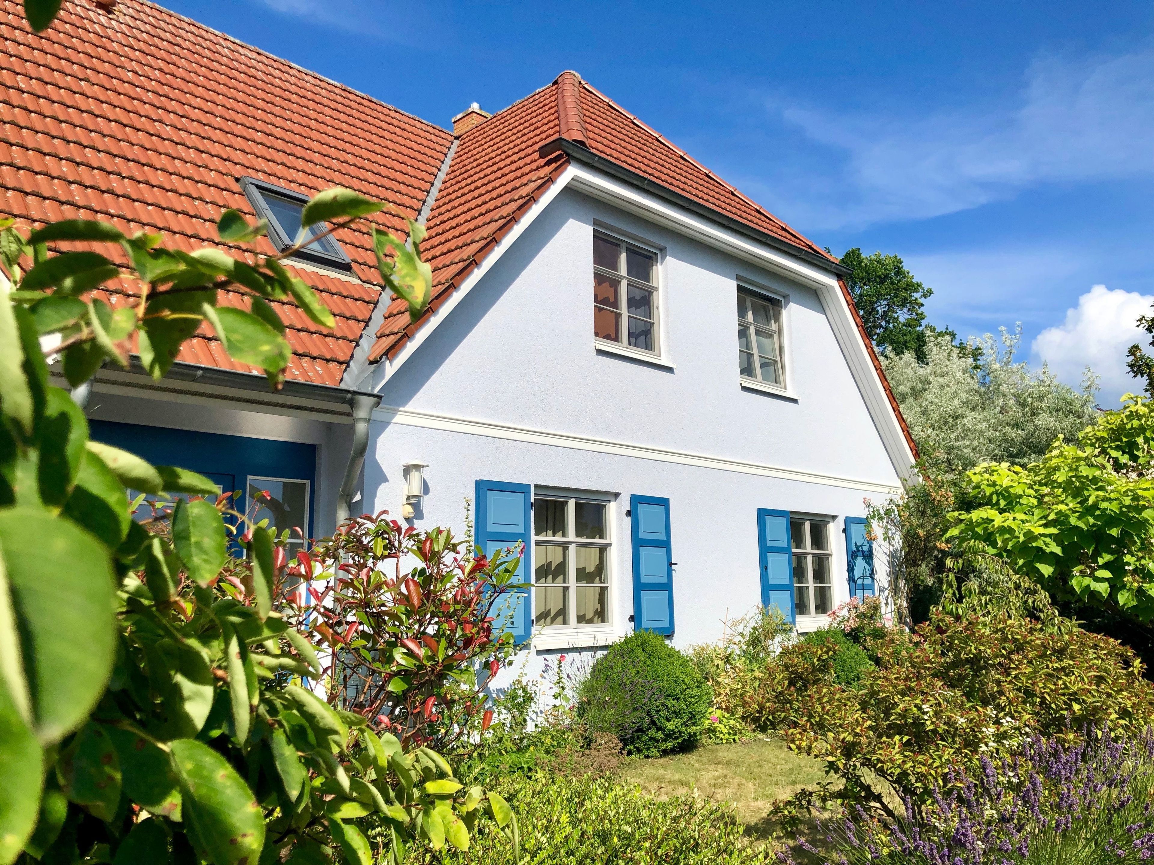 A two-story house with a red-tiled roof, white walls, and blue shutters.