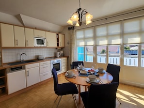 A kitchen with a dining table set for four, a microwave, oven, and a coffee maker. - Abels Strandkoje, Germany (Wustrow)