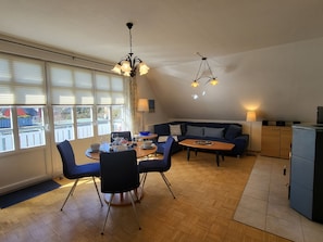 A dining area with a table, chairs, and a chandelier. There is a sofa and a small kitchen area with cabinets.