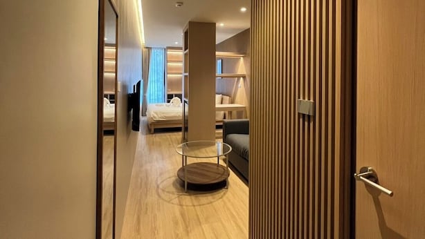 Een moderne hotelgang met een houten deur, een ronde tafel en een bed op de achtergrond.