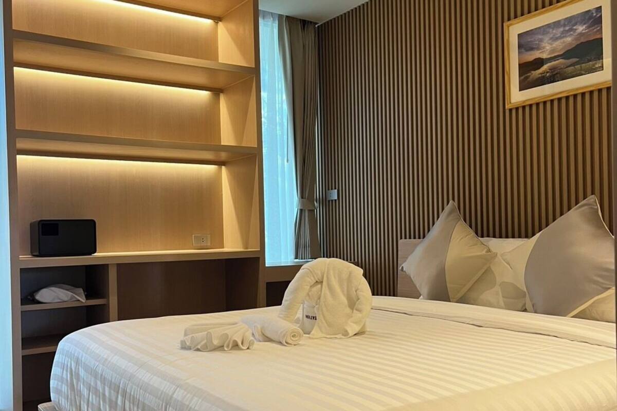 A modern hotel room with a large bed, a wooden headboard, a flat-screen TV, and a painting on the wall.