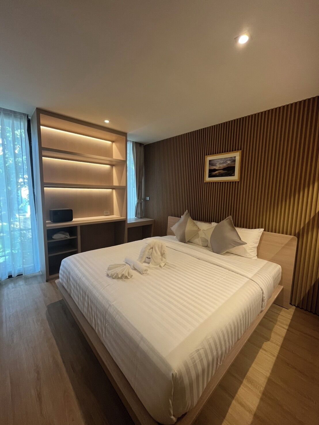 A modern hotel room with a large bed, a built-in wardrobe, and a bedside table.