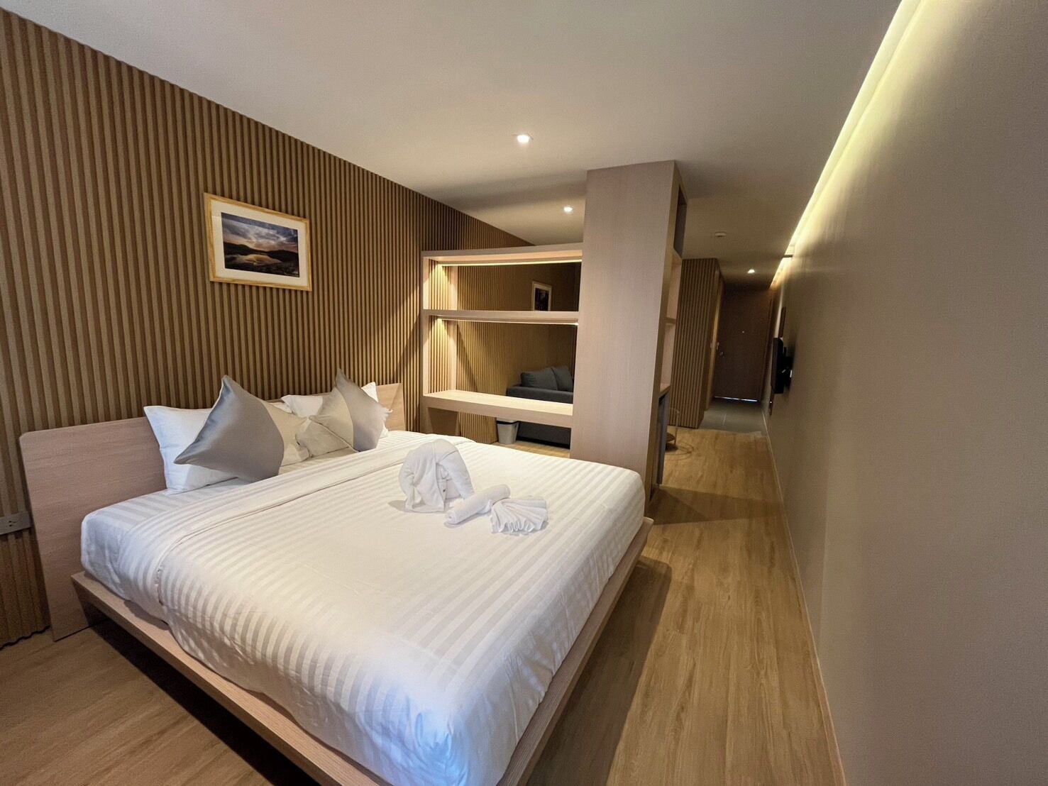 Ein modernes Hotelzimmer mit einem großen Bett, Holzvertäfelung an den Wänden, einem integrierten Schreibtisch und Blick auf den Flur.