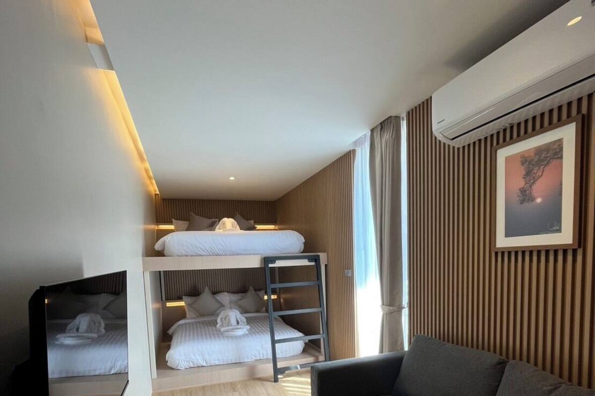 A modern hotel room with a bunk bed, a sofa, a glass coffee table, and a mounted TV.