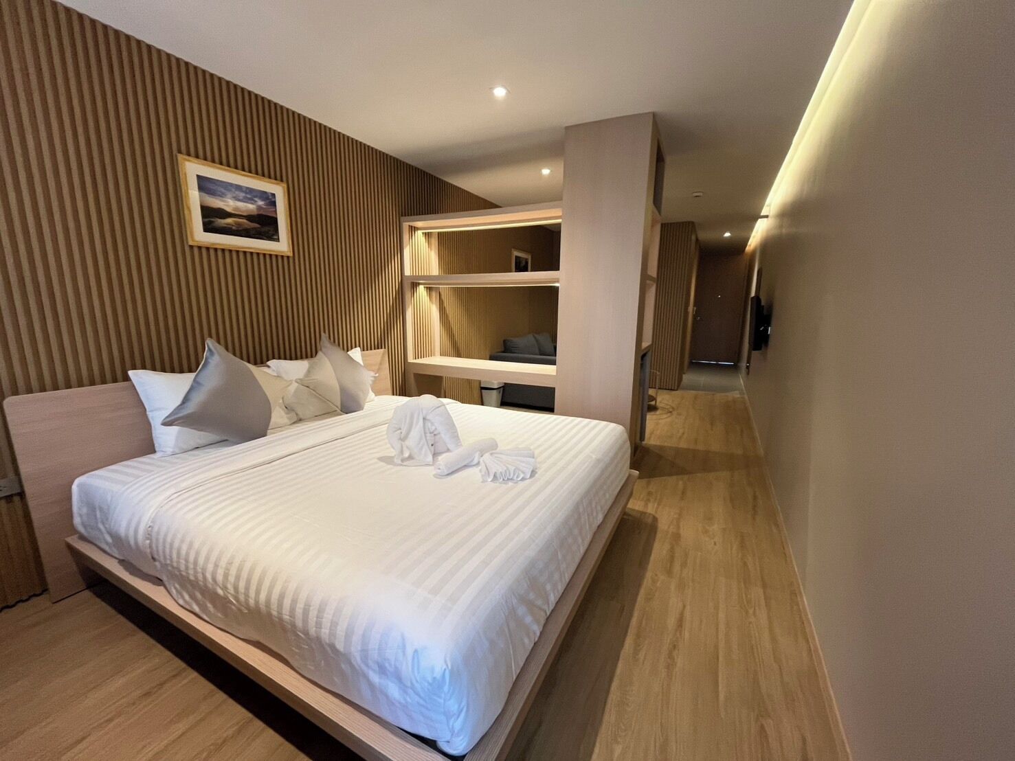 Habitació d'hotel moderna amb un llit gran, un panell frontal de fusta, una taula de nit i un moble prestatge integrat.