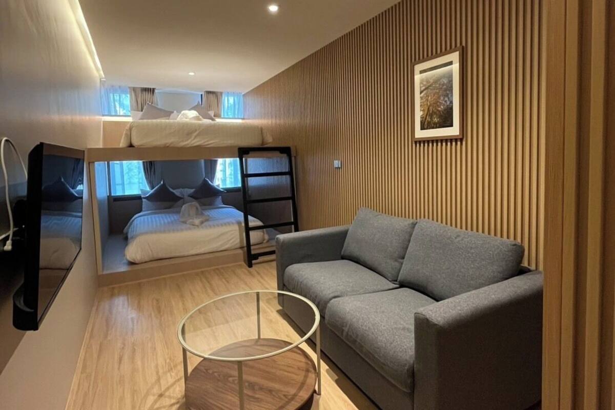A modern room with a bunk bed, a grey sofa, a round glass coffee table, and wooden paneling on the walls.