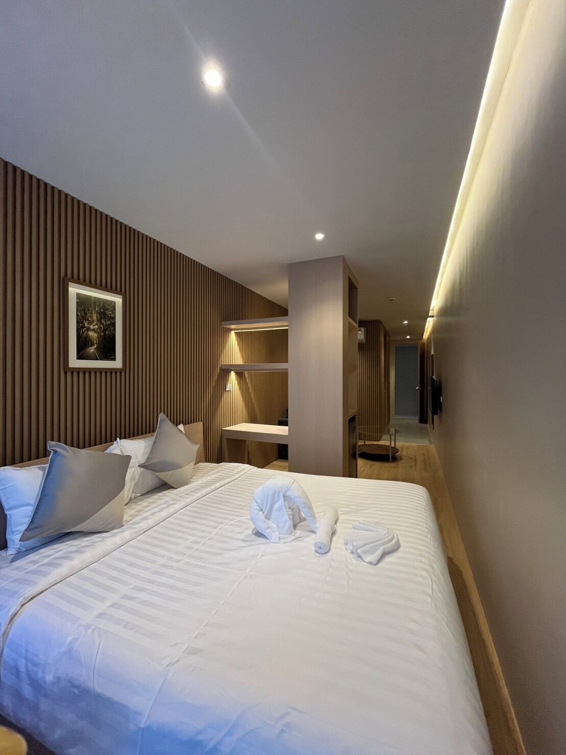 Una habitación de hotel moderna con una cama grande, una mesita de noche, un espejo y un televisor de pared.