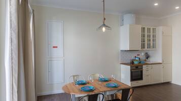 Uma sala de jantar com mesa de madeira posta para quatro pessoas, cozinha com armários brancos e luminária pendente.