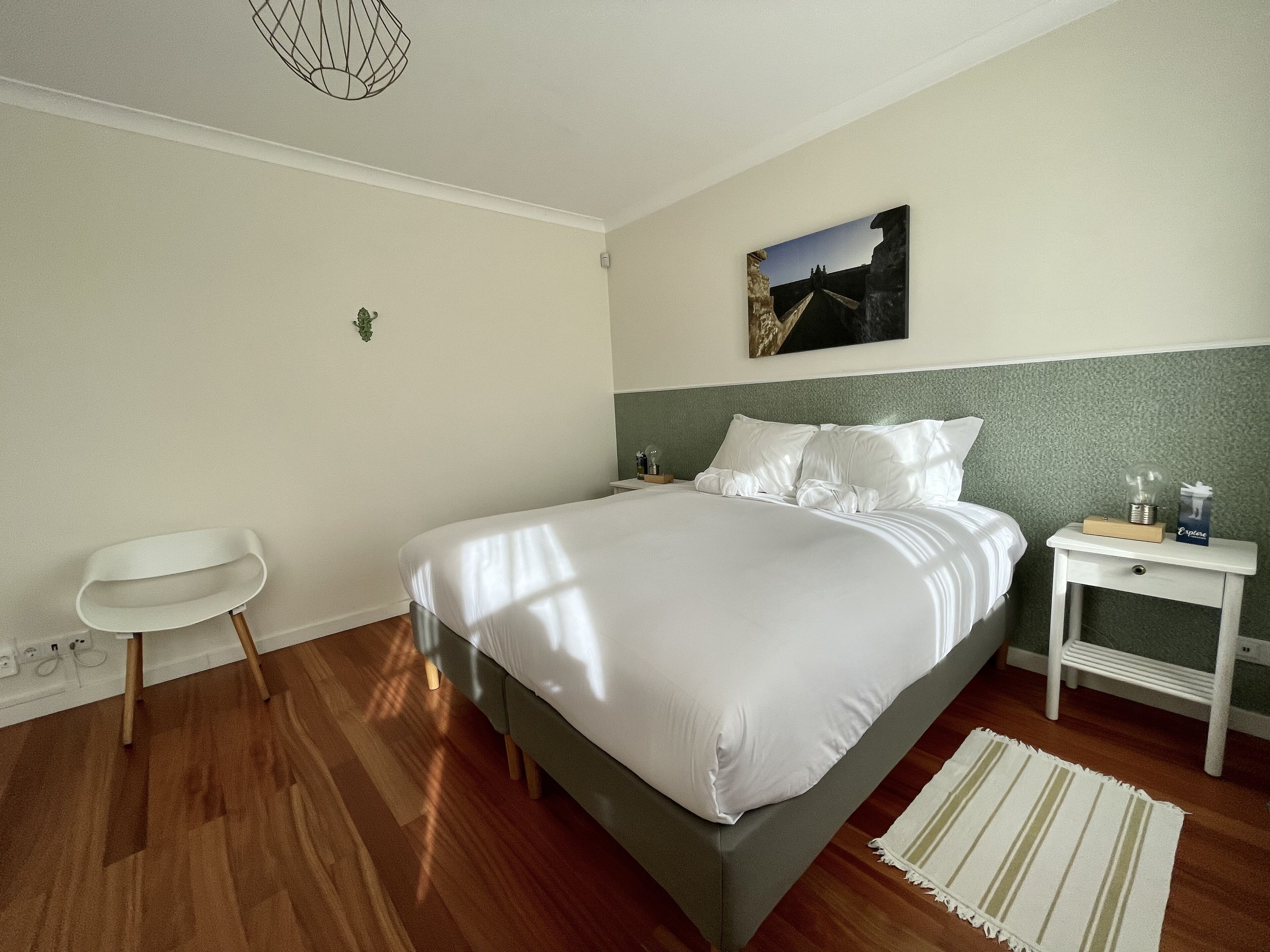 A modern bedroom with a large bed, a chair, a nightstand, and a painting on the wall.